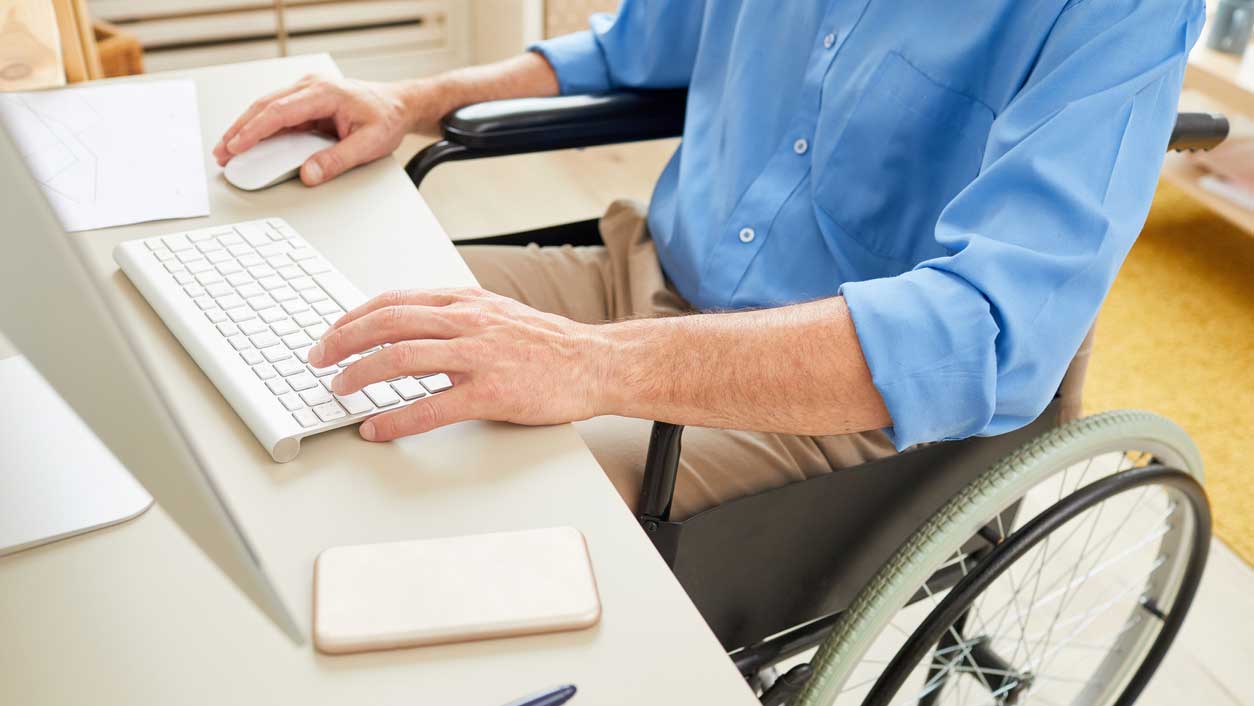Man with disabilities sitting in a wheelchair while using a computer - an idea of ADA website compliance